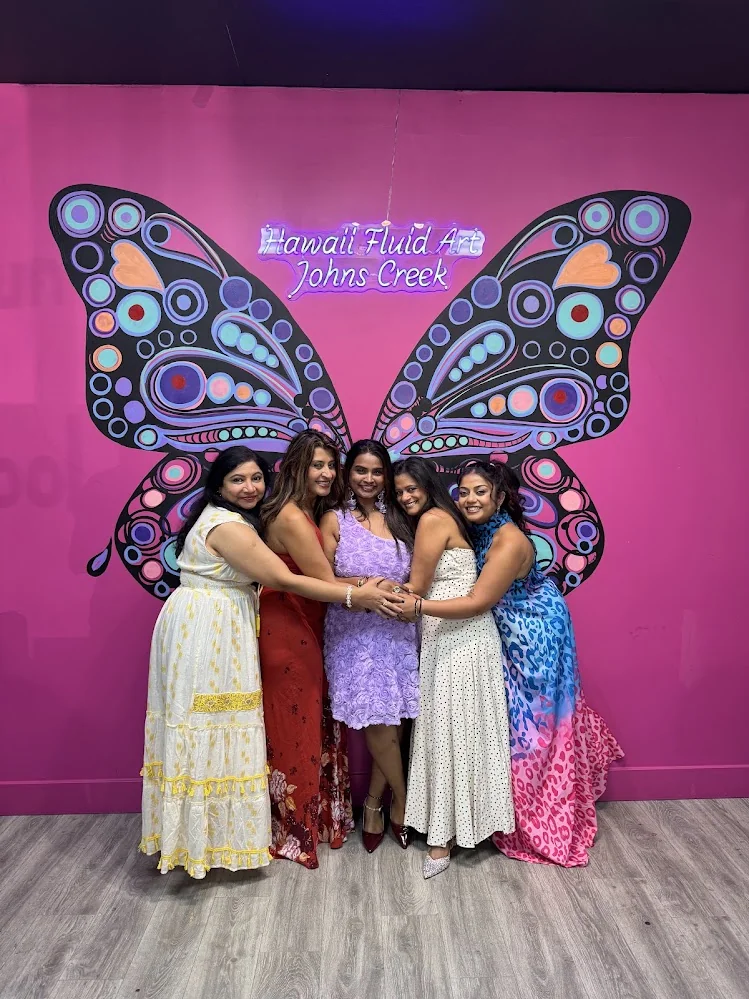 Ladies celebrating a fun kitty party in front of the neon butterfly art wall at Hawaii Fluid Art Johns Creek